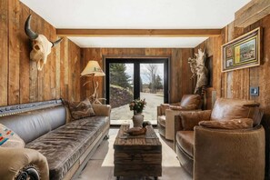 Ein rustikales Interieur mit Holzwänden, Ledermöbeln, einem großen Fenster und einem aufgehängten Tierkopf.