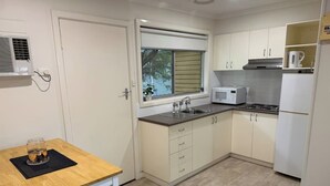 A compact kitchen with a window, white cabinets, a microwave, and a sink. - Froggy’s Quarters Cabin 5 - Koala (Halls Gap)