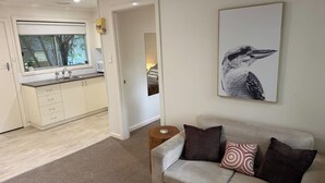 A living room with a sofa, a coffee table, and a framed picture on the wall. - Froggy’s Quarters Cabin 5 - Koala (Halls Gap)