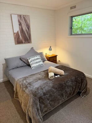 Ein Schlafzimmer mit einem Bett, Kissen, einer Nachttischlampe, einem Fenster und einem Wandbild.