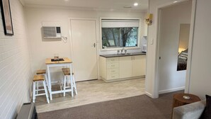A compact living space with a kitchenette, a dining area with a table and chairs, and a seating area with a sofa. - Froggy’s Quarters Cabin 5 - Koala (Halls Gap)
