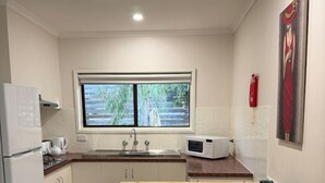 Cocina compacta con ventana, armarios blancos, microondas y una mesa de madera con bancos.