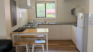 A compact kitchen with a window, white cabinets, a microwave, and a refrigerator. - Froggy’s Quarters Cabin 9 - Wombat (Halls Gap)