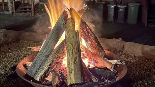 A fire pit with logs, surrounded by gravel, with a building and stairs in the background. - Froggy’s Quarters Cabin 9 - Wombat (Halls Gap)