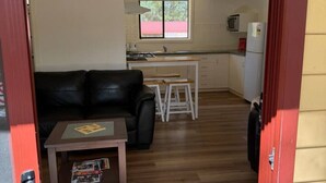 A compact living space with a kitchenette, a dining area, and a seating area with a sofa and a small table. - Froggy’s Quarters Cabin 9 - Wombat (Halls Gap)