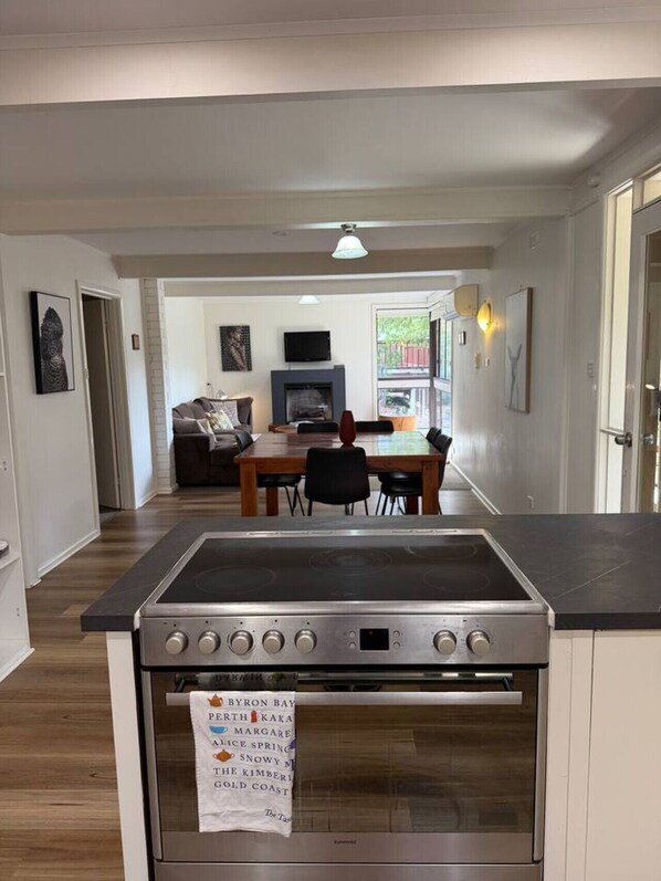 A modern kitchen with a built-in stove, a dining area with a table and chairs, and a living room with a sofa and fireplace.
