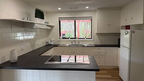 A modern kitchen with white cabinets, a black countertop, a built-in stove, and a window with a view of greenery. - Froggy`s Quarters Cabin 1 - Cockatoo (Halls Gap)