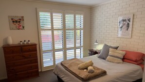 A bedroom with a bed, a dresser, a window with blinds, and a wall-mounted picture. - Froggy`s Quarters Cabin 1 - Cockatoo (Halls Gap)
