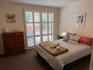 Ein Schlafzimmer mit Bett, Kommode, einem Fenster mit Jalousien und einem Wandbild.