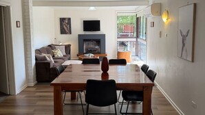 A spacious living area with a fireplace, a dining table with chairs, a sofa, and a television. - Froggy`s Quarters Cabin 1 - Cockatoo (Halls Gap)