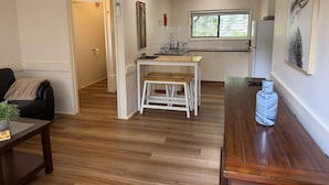 A modern kitchen with white cabinets, a wooden dining table, and a bench. - Froggy’s Quarters Cabin 3 - Emu (Halls Gap)
