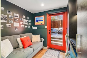 Ein Wohnzimmer mit grauem Sofa, rotem Tür und einer Wand mit Schwarz-Weiß-Fotos.