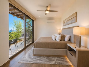 A bedroom with a bed, bedside lamps, a ceiling fan, and a view of greenery and mountains. - Casa Vista 133 · Private Luxury Villa w/ Rooftop Views in Cabo (Cabo San Lucas)