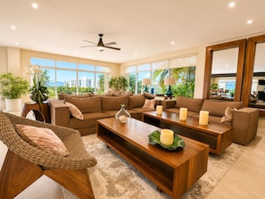 A modern living room with a sectional sofa, a wooden coffee table, and a wicker chair. - Casa Vista 133 · Private Luxury Villa w/ Rooftop Views in Cabo (Cabo San Lucas)