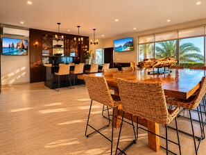 A modern kitchen with a dining area, large windows, and a view of the ocean. - Casa Vista 133 · Private Luxury Villa w/ Rooftop Views in Cabo (Cabo San Lucas)