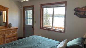 Une chambre à coucher comprenant un lit, une commode, un ventilateur de plafond, deux fenêtres et une vue sur un lac.
