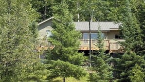 Une cabane avec un quai, entourée d’arbres et bordée par un plan d’eau.