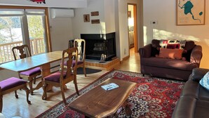 Un salon avec une cheminée, des meubles en bois, un tapis rouge à motifs et une carte accrochée au mur.