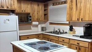 Une cuisine avec des meubles en bois, un réfrigérateur blanc, un four à micro-ondes, une cuisinière, un évier et une machine à café.
