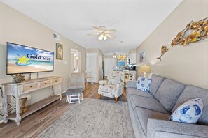 Ein Wohnzimmer mit Fernseher, der 'Gold Star Vacation Rentals' anzeigt, einem Deckenventilator, einem Sofa, einem Couchtisch und einem Essbereich im Hintergrund.