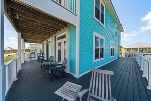 A covered deck with outdoor furniture, a wooden bench, and a house with a blue exterior. - Dog Friendly Beach House 200ft from the Beach (Gulf Shores)