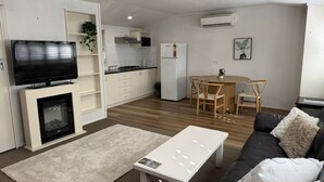 A modern living room with a fireplace, a TV, a dining area with a table and chairs, and a kitchen area with a refrigerator and cabinets.