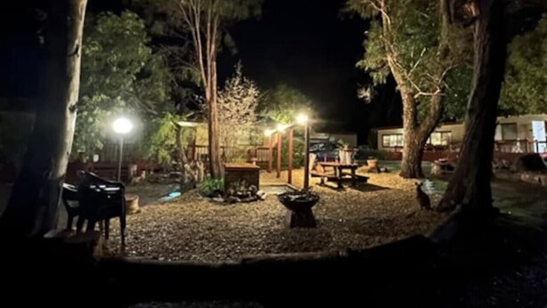 A nighttime outdoor area with a gazebo, seating, and a fire pit.
