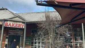 A bakery with a signboard, a person standing at the entrance, and a bird perched on the awning. - Froggy’s Quarters Cabin 8 - Possum (Halls Gap)