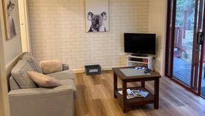 A living room with a grey sofa, a coffee table, a flat-screen TV, and a framed picture of a koala on the wall. - Froggy’s Quarters Cabin 8 - Possum (Halls Gap)