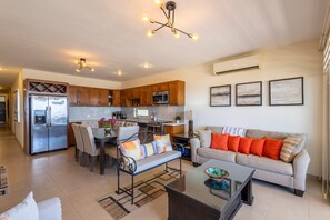 Eine moderne Küche mit integrierten Geräten, ein Essbereich mit einer Bank und ein Wohnzimmer mit Sofa und Couchtisch.