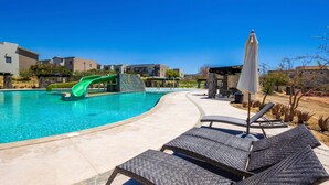Une piscine avec un toboggan, des chaises longues et un parasol.