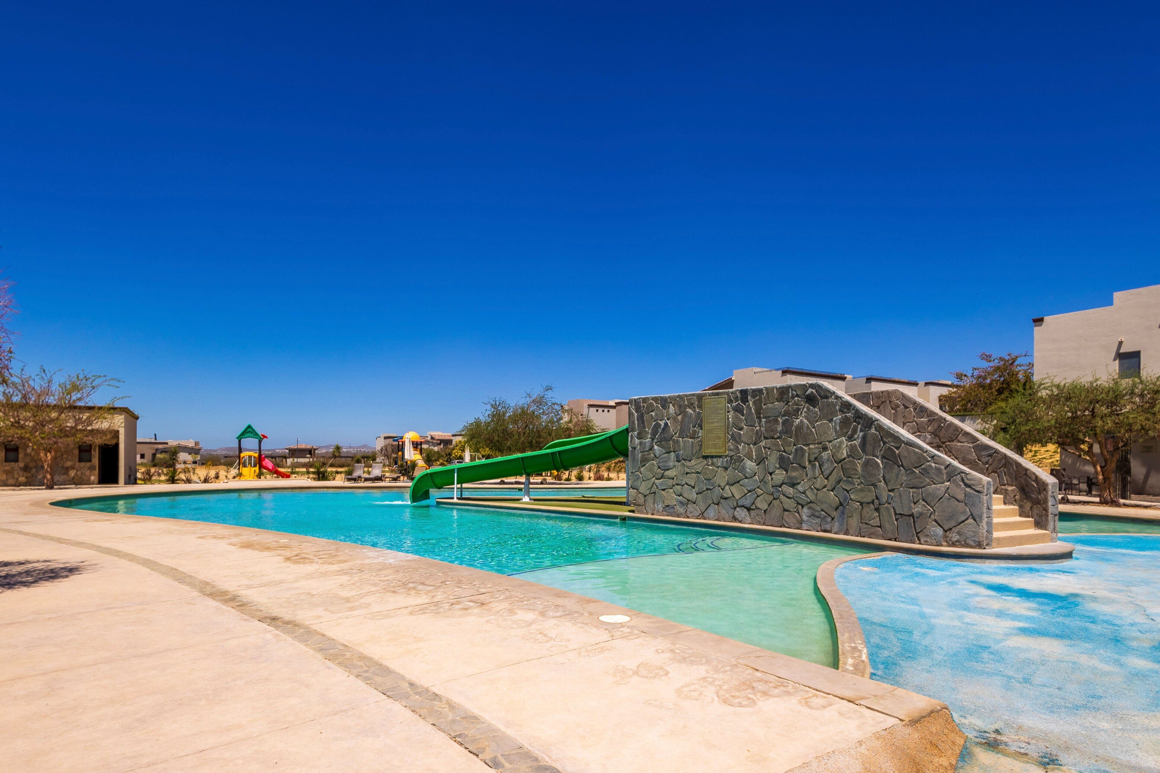 Ein Schwimmbecken mit einer grünen Rutsche, Steinwänden und einem strahlend blauen Himmel.
