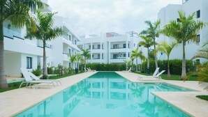 Una piscina con sillas de descanso, rodeada de palmeras y edificios modernos.