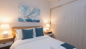 Habitación de hotel con cama, dos lámparas de noche, un cuadro de un velero y un aire acondicionado.