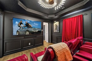 Ein Heimkino mit großem Flachbildfernseher, roter Lederausstattung und einer Deckenleuchte.