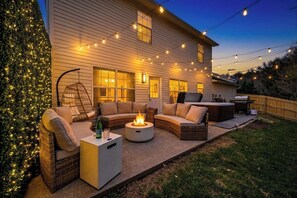 Une maison dotée d’un patio aménagé avec des meubles d’extérieur, un foyer et des guirlandes lumineuses.