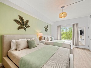 Ein Schlafzimmer mit zwei Betten, einer Hängelampe, einem Fenster mit Vorhängen und einem an der Wand montierten Fernseher.