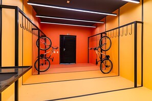 Una habitación luminosa de paredes naranjas, con una puerta negra, dos bicicletas colgadas en las paredes y una escalera con barandillas negras.