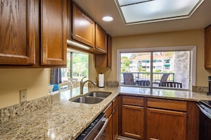 A kitchen with granite countertops, wooden cabinets, a built-in dishwasher, and a window overlooking a balcony. - Lagoon Views; Community Pool, Hot Tub & Cabana; Dog-Friendly; Walk to Shelter Cove Marina & Shops! (Hilton Head Island)