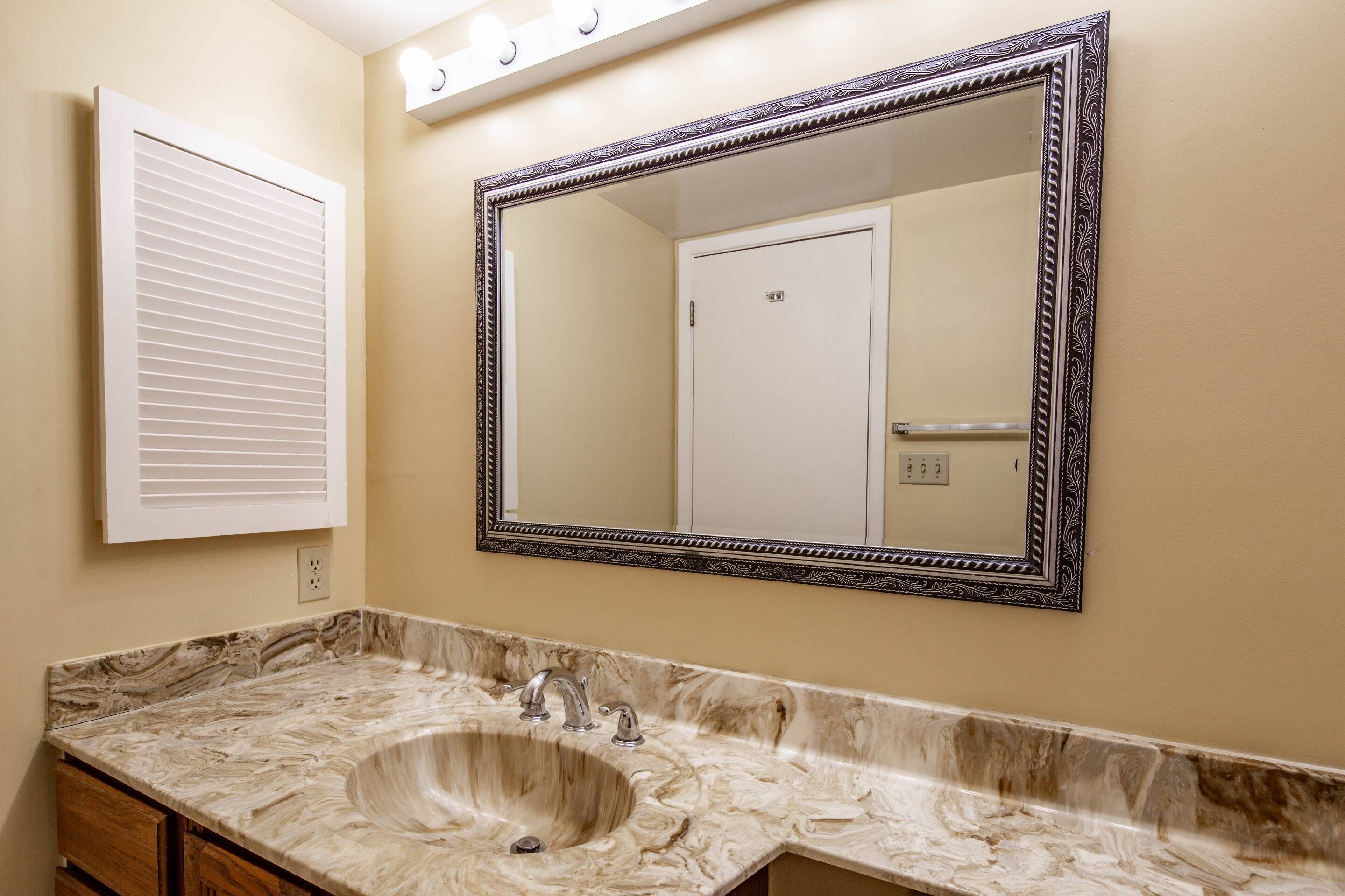 Une salle de bain avec un lavabo en marbre, un grand miroir et une porte blanche.