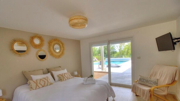 A bedroom with a bed, a chair, and a view of a swimming pool. - Villa Ambre - BULLY - Gîte (BULLY)