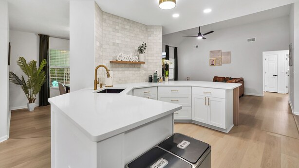 Una cocina moderna con armarios blancos, una isla central y un ventilador de techo.