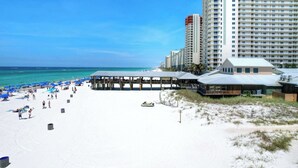 Uma praia com um píer, área com guarda-sóis e edifícios altos ao fundo.