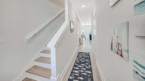 Um corredor com escadas, um tapete com padrão de peixes azuis e um quadro de um veleiro na parede.