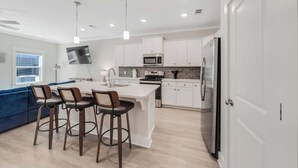 Cozinha moderna com armários brancos, uma ilha central com banquetas, micro-ondas embutido e geladeira.
