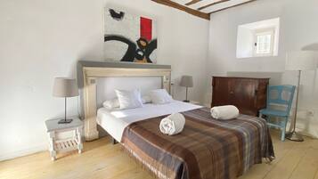 A bedroom with a bed, two bedside tables, a wooden headboard, a painting, a window, and a blue chair.