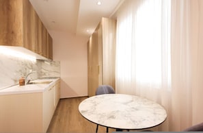 A modern kitchen with marble countertops, wooden cabinets, and a round marble table. - Cozy Apartment 04 in Durr s (Durrës)