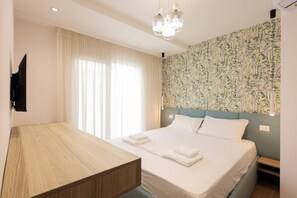 Quarto de hotel com cama, escrivaninha de madeira, TV fixada na parede e cabeceira com padrão floral.
