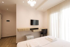 Quarto de hotel com cama, escrivaninha, cadeira, televisão e um pequeno cesto de lixo.