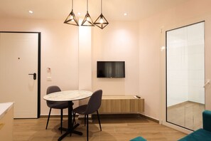 Ein modernes Zimmer mit einem runden Tisch, zwei Stühlen, einem an der Wand montierten Fernseher und einer Schiebetür aus Glas.